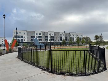 A black fence surrounds a grassy area in front of a white building.